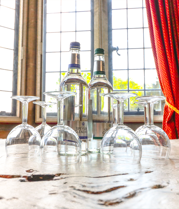 Bottles of water and wine glasses sat on a wooden table with windows in the background.