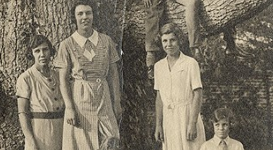 An old black and white photograph of a family sat around a tree.