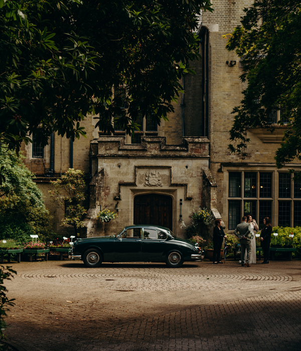 A vintage car placed in front of Minstead Lodge with a bride and events team standing beside her