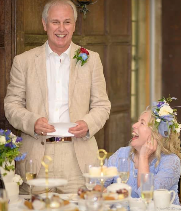 A man standing giving a speech at an event with a woman smiling up at him.