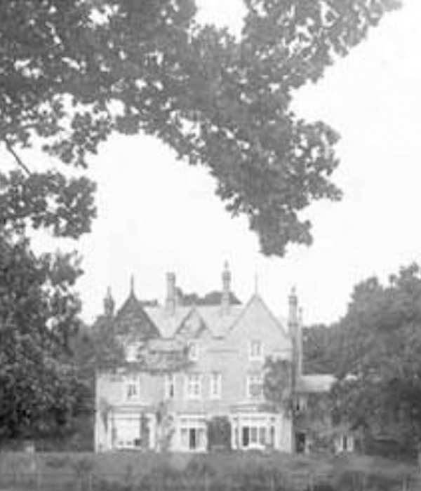 An old black and white photograph of Minstead Lodge taken from a distance with trees in the background.