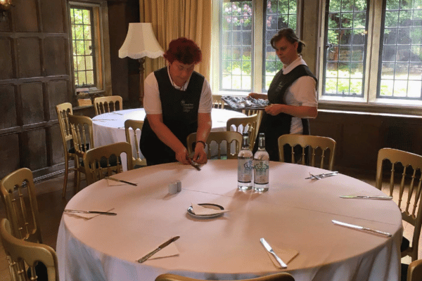 Two people preparing a table for a conference in the Long Hall at Minstead Lodge.