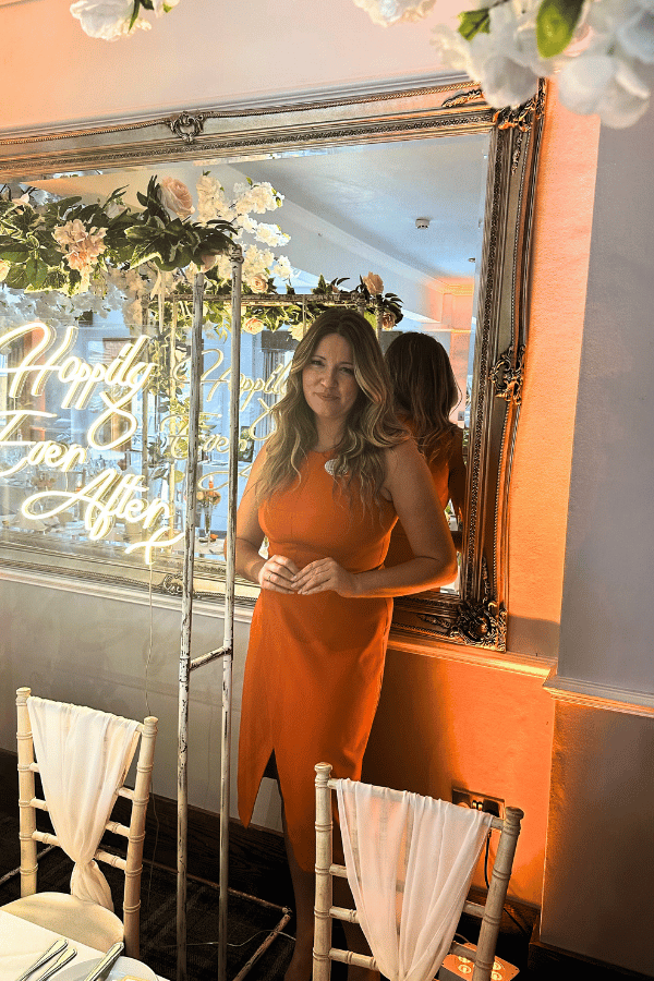 Woman wearing an orange dress in front of a mirror at a wedding.