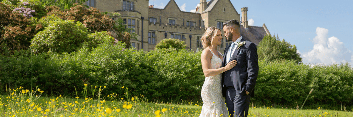 Bride and groom standing in a field with yellow flowers, with Minstead Lodge in the background