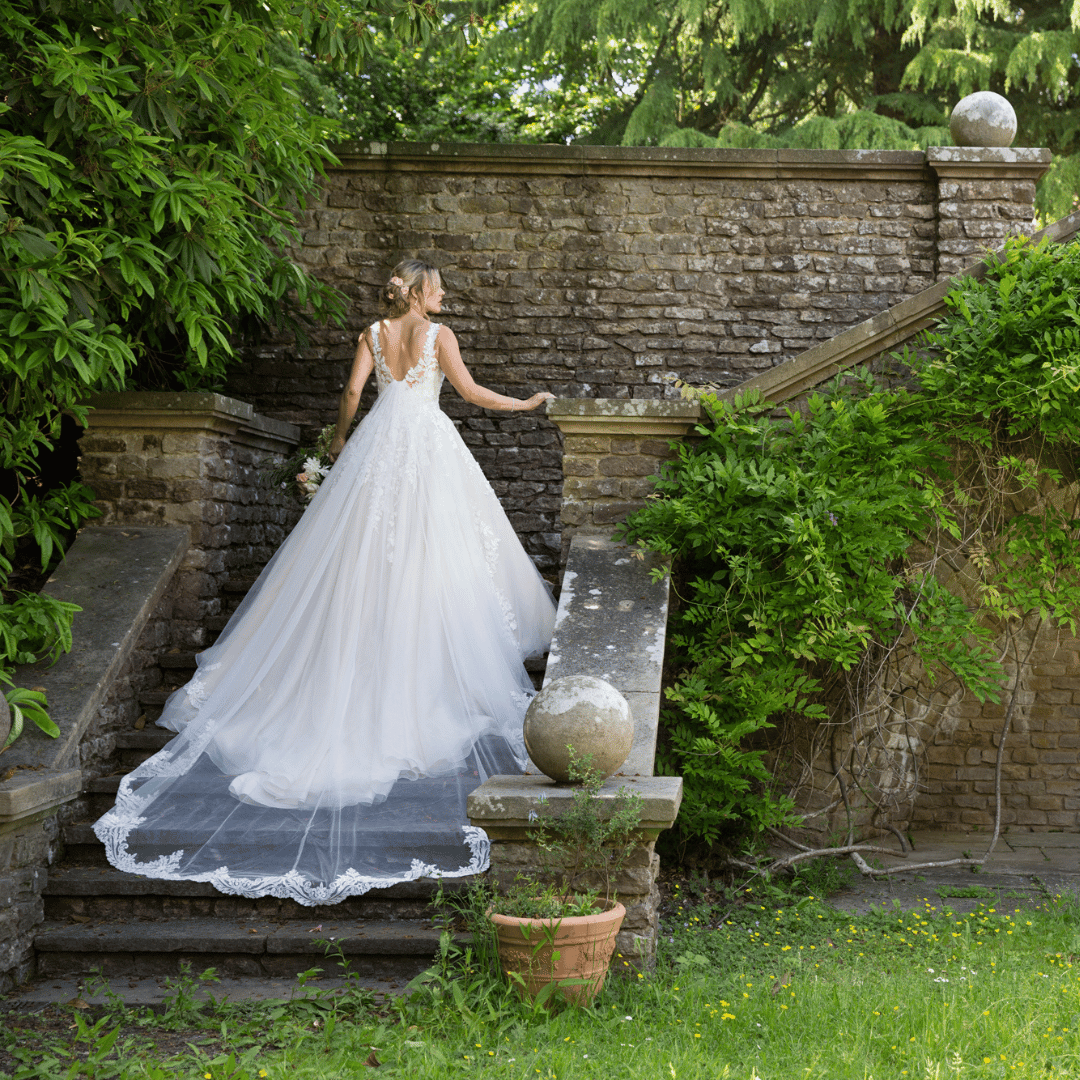 A bride walking up some stone stairs outdoors, with her wedding dress trailing behind her