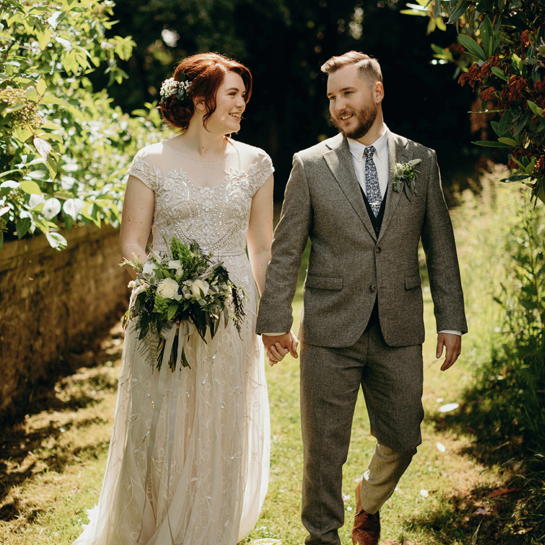 A wedding couple walking towards the camera outdoors holding hands.