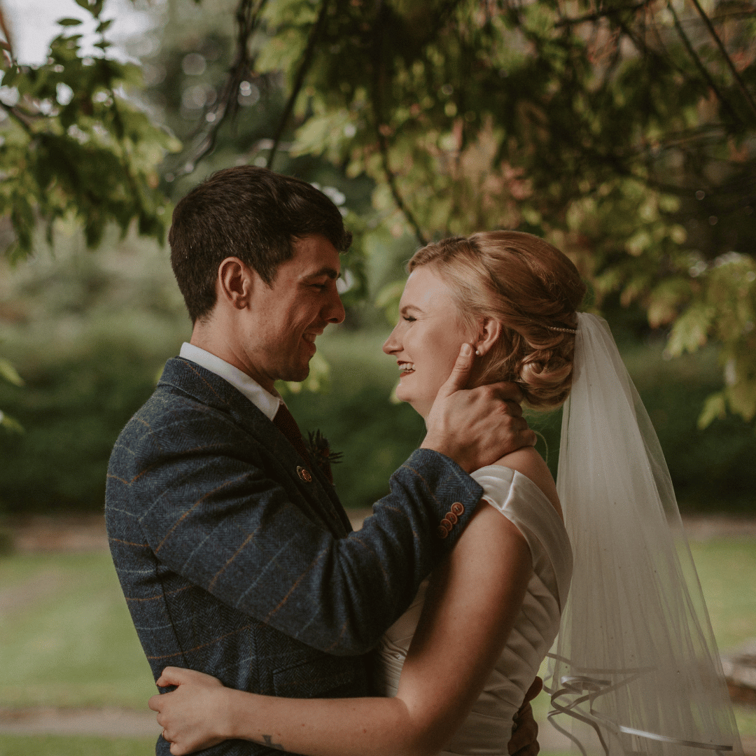 Bride and groom hugging outdoors after their wedding ceremony. Trees are in the background.